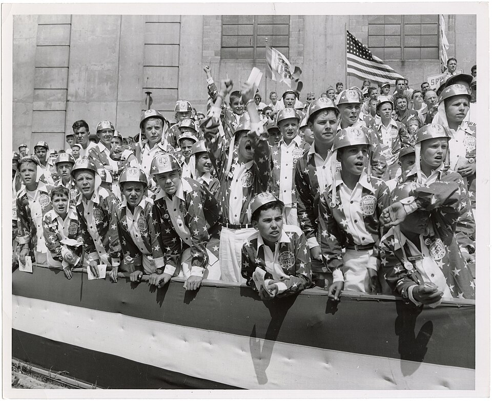 Young 1952 Soap Box Derby city champions in star-pattern uniforms cheering from a crowded railing outside Akron's Rubber Bowl