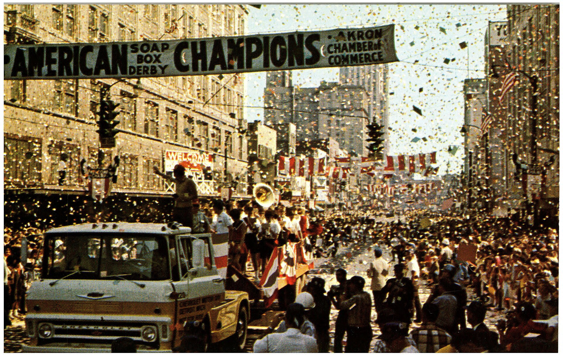 Confetti, parade vehicles, flags, banners, and dense crowds filling downtown Akron to welcome Soap Box Derby champions