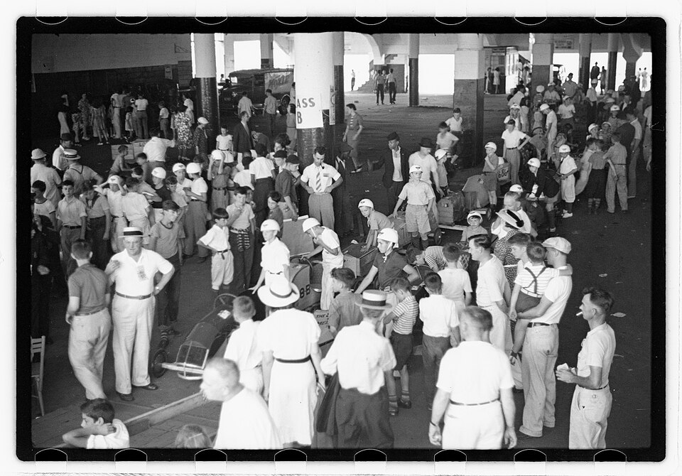 Busy indoor 1938 Soap Box Derby paddock filled with handmade cars, young racers, families, and officials in Boston