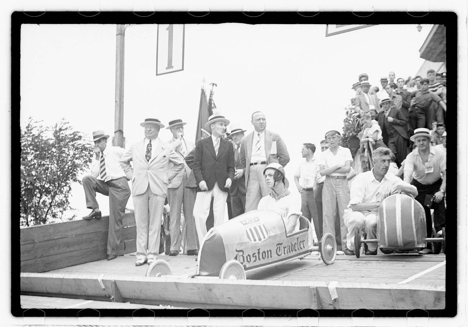 Two racers seated in streamlined newspaper-sponsored Soap Box Derby cars at a crowded Boston starting ramp in 1938